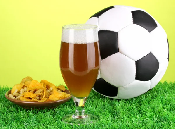 Glass of beer with soccer ball on grass on green background