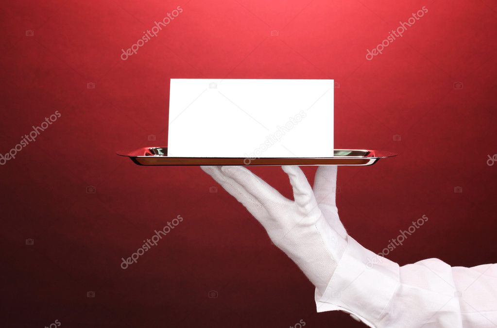 Hand in glove holding silver tray with blank card on red background