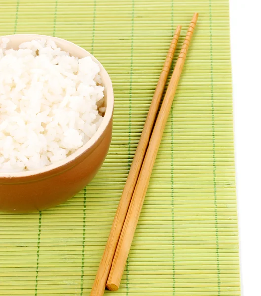 Чаша риса и палочки для еды на бамбуковом коврике, изолированном на белом — стоковое фото