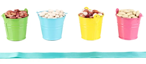 Diferentes tipos de feijões em baldes coloridos isolados em branco — Fotografia de Stock