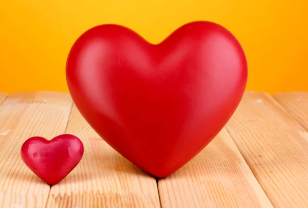 Dekorative rote Herzen auf Holztisch auf orangefarbenem Hintergrund — Stockfoto