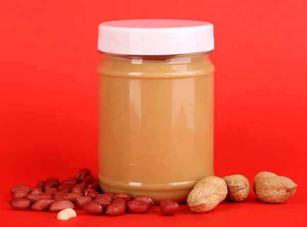 Delicious peanut butter in jar of peanut near on red background — Stock Photo, Image