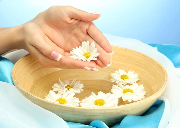 Manos de mujer con cuenco de madera de agua con flores, sobre fondo azul —  Fotos de Stock