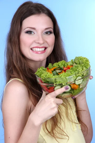 Hermosa mujer con ensalada de verduras sobre fondo azul — Foto de Stock