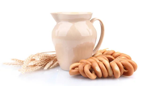 Pot van melk, smakelijke bagels en spikelets, geïsoleerd op wit — Stockfoto
