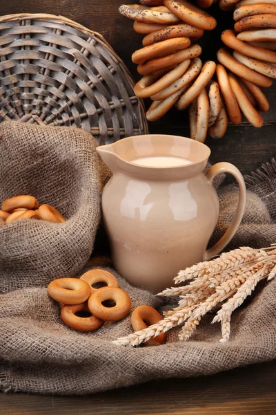 Jar of milk, tasty bagels and spikelets on wooden background — Stock Photo, Image