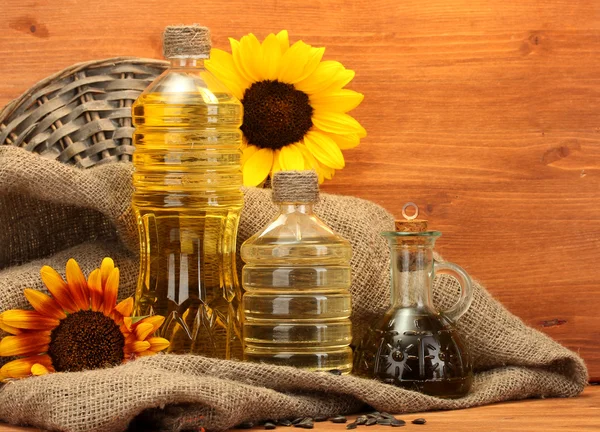 Oil in bottles, sunflowers and seeds, on wooden background — Stock Photo, Image