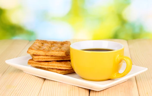 Xícara de café e biscoitos na mesa de madeira no fundo brilhante — Fotografia de Stock