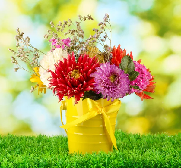 Ljust gul hink med blommor på grön bakgrund — Stockfoto
