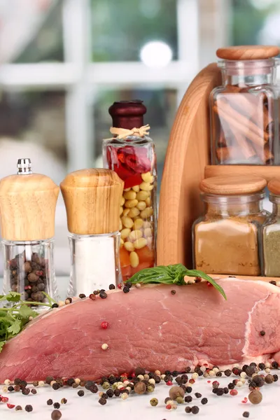 Een groot stuk van varkensvlees gemarineerd met kruiden en specerijen op witte tafel op achtergrond van venster — Stockfoto