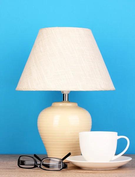 Table lamp with cup and glasses on blue background — Stock Photo, Image