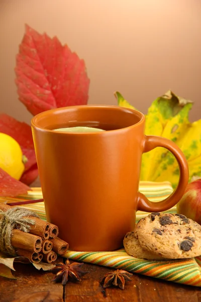 Tazza di tè caldo e foglie autunnali, su sfondo marrone — Foto Stock