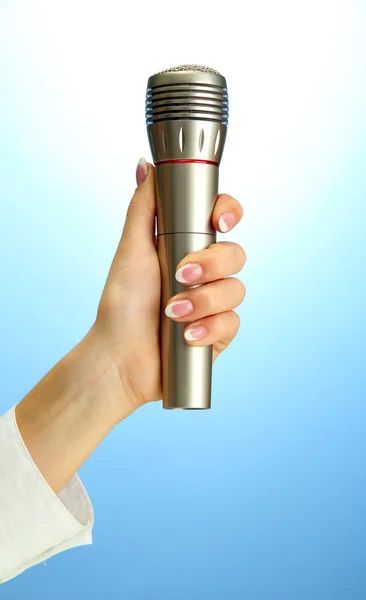 Mão feminina com microfone, no fundo azul — Fotografia de Stock