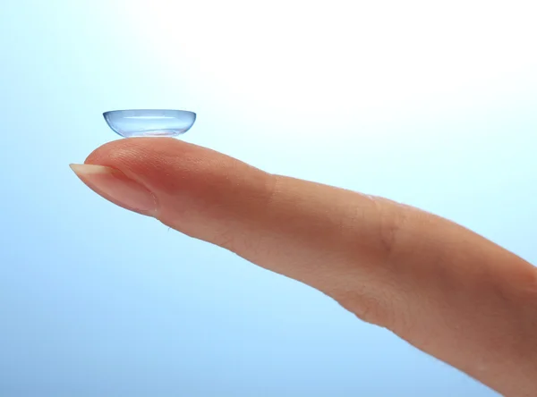 Contact lens op vinger op blauwe achtergrond — Stockfoto