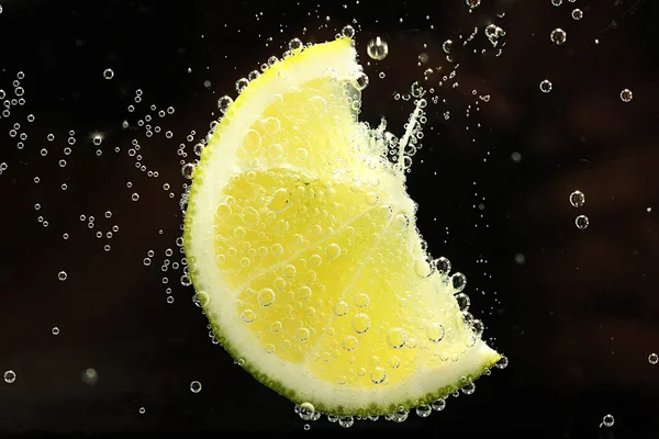 Fatia de limão na água com bolhas, sobre fundo preto — Fotografia de Stock