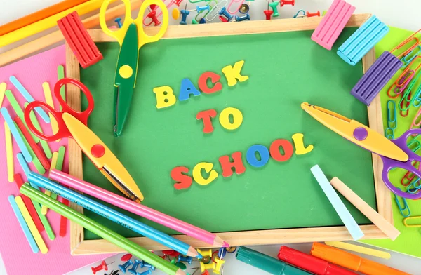 Piccola lavagna con materiale scolastico su fondo bianco. Torna a scuola — Foto Stock