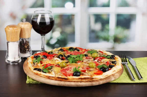 Delicious pizza with glass of red wine and spices on wooden table on window background — Stock Photo, Image