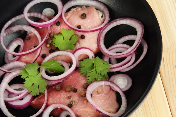 Un morceau de porc avec des oignons frits dans une casserole close-up sur une table en bois — Photo