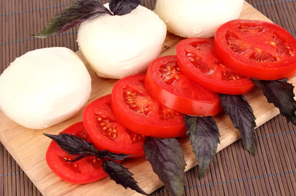 Gustosa mozzarella con pomodori sul tagliere sul tappetino — Foto Stock