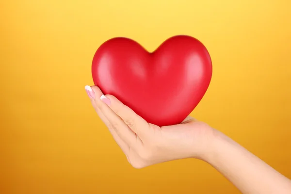 Rotes Herz in Frauenhand, auf orangefarbenem Hintergrund Nahaufnahme — Stockfoto