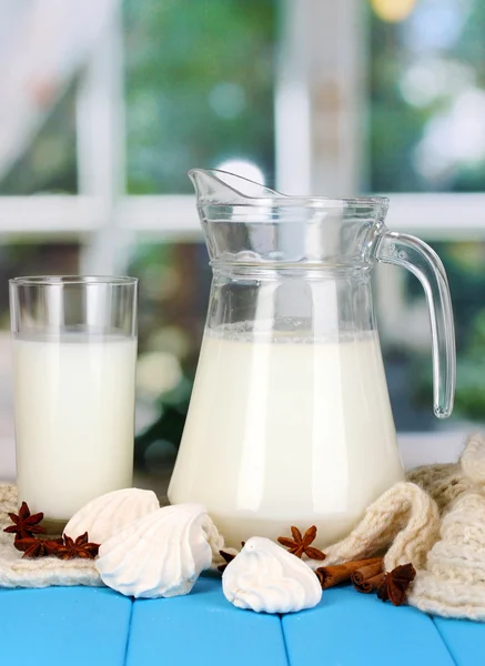 Jarra y vaso de leche con merengues en punto de cuello redondo sobre mesa de madera sobre fondo de ventana — Foto de Stock