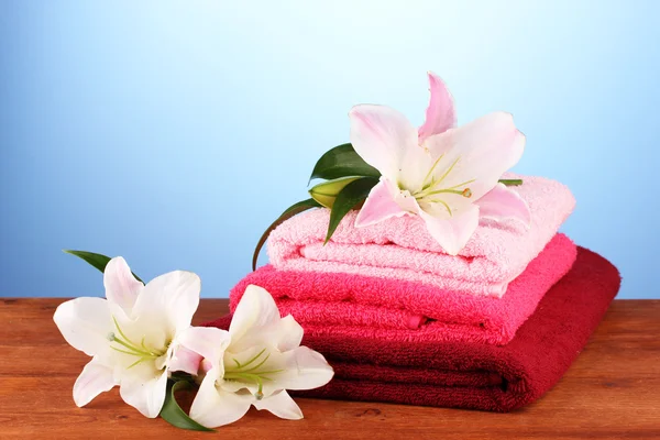 Stack of towels with pink lily on blue background — Stock Photo, Image