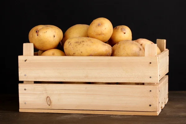 Reife Kartoffeln in Holzkiste auf Holztisch auf schwarzem Hintergrund — Stockfoto