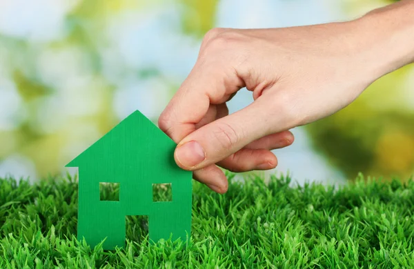 Ręka trzyma papier domu na zielonym tle, bliska — Zdjęcie stockowe