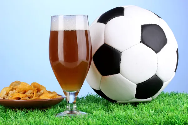 Copo de cerveja com bola de futebol na grama no fundo azul — Fotografia de Stock