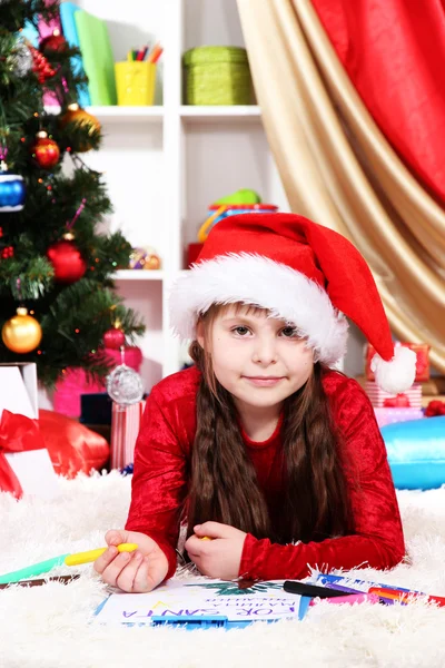 Красивая маленькая девочка пишет письмо Санта-Клаусу в празднично украшенной комнате — стоковое фото