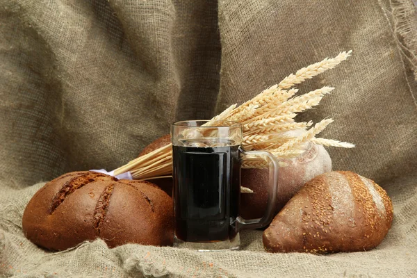 Tankard of kvass and rye breads with ears, on burlap background — Stock Photo, Image