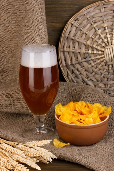 Glass of beer with plate of chips on wooden table on sacking background — Stock Photo, Image
