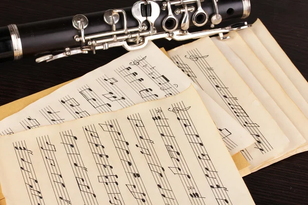 Musical notes and clarinet on wooden table — Stock Photo, Image