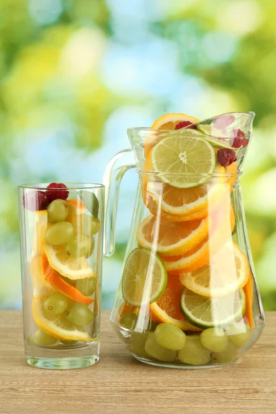 Kruik en glas met citrusvruchten en frambozen, op groene achtergrond — Stockfoto