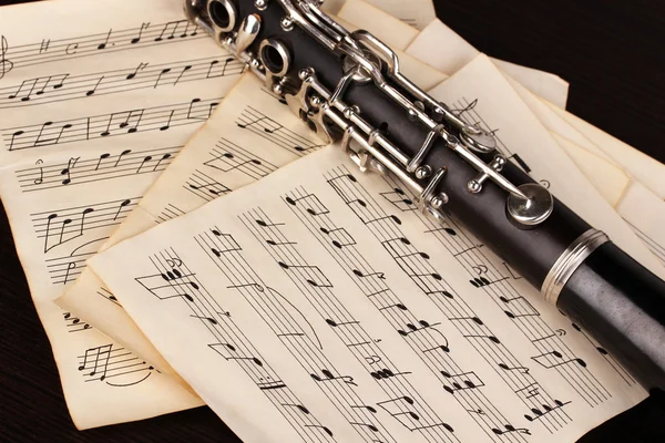 Musical notes and clarinet on wooden table — Stock Photo, Image