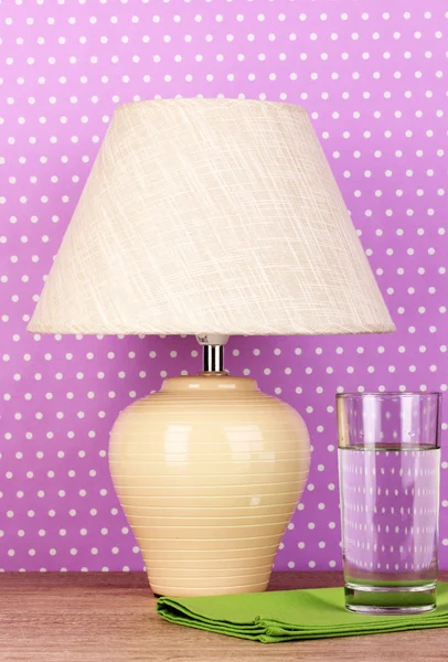 Table lamp and glass of water on purple polka dot background — Stock Photo, Image