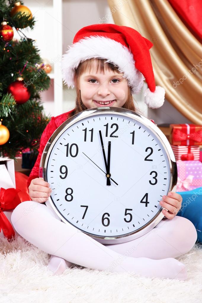 Beautiful little girl with clock in anticipation of New Year in festively decorated room