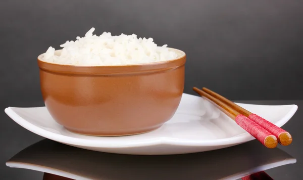 Tigela de arroz e pauzinhos no prato em fundo cinza — Fotografia de Stock