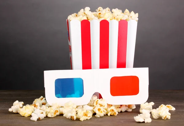 Popcorn e bicchieri da cinema su tavolo in legno su sfondo grigio — Foto Stock