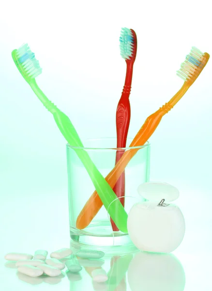 Toothbrush in glass, dental floss and chewing gum on green background — Stock Photo, Image