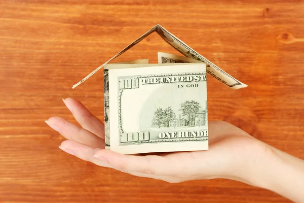 Hand holding een huis gemaakt van dollars op houten achtergrond close-up — Stockfoto