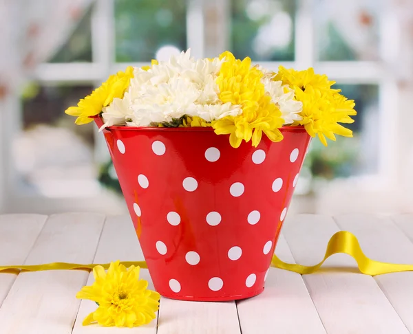 Red pail of peas with flowers on white wooden table on window background — Stock Photo, Image