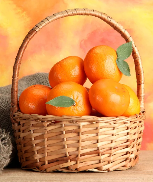 Tangerines με αφήνει σε ένα όμορφο καλάθι, στο ξύλινο τραπέζι σε πορτοκαλί φόντο — Φωτογραφία Αρχείου