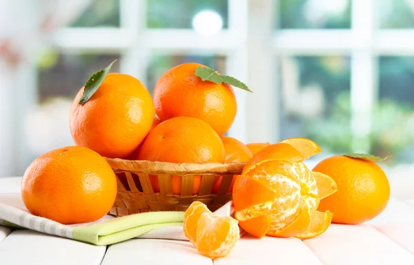 Tangerines with leaves in a beautiful basket, on wooden table on window background — Stock Photo, Image
