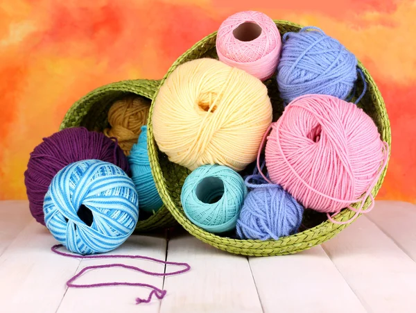 Colorful yarn for knitting in green basket on white wooden table on colorful background — Stock Photo, Image
