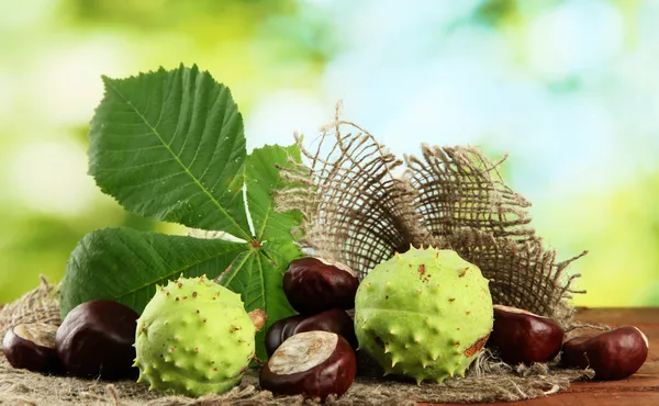 Castanhas com folhas na mesa de madeira em fundo verde — Fotografia de Stock