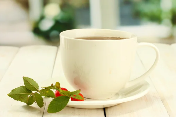 Tasse Tee mit Hüftrosen, auf Holztisch — Stockfoto