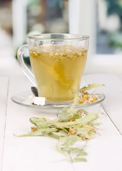 Glass cup of tea with linden on wooden table on window background — Stock Photo, Image