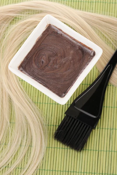 Tintura per capelli in ciotola e pennello per la colorazione dei capelli su tappetino di bambù verde, primo piano — Foto Stock