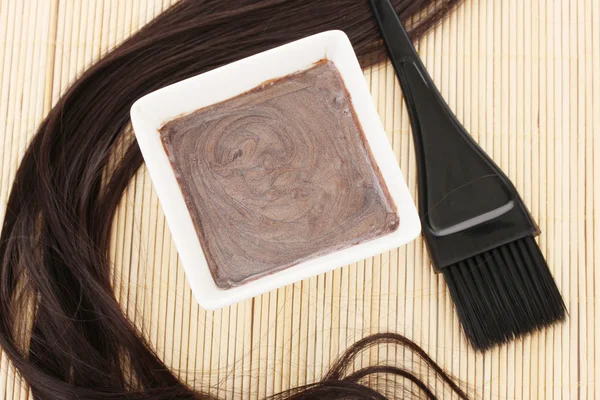Tintura per capelli in ciotola e pennello per la colorazione dei capelli su tappetino di bambù beige, primo piano — Foto Stock